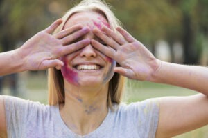 Femme souriante, cachant son visage tâché de peinture avec ses mains lors d'un atelier artistique